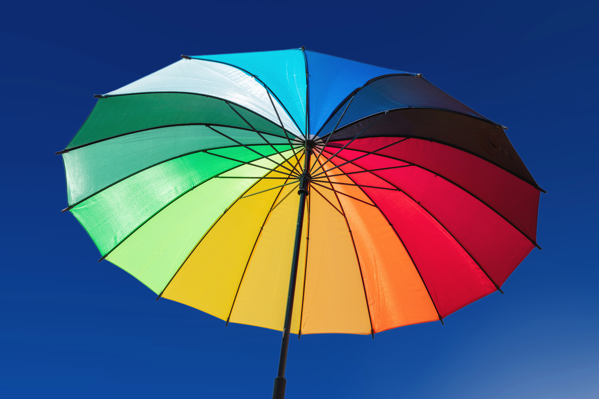 Rainbow colors umbrella against blue sky background, sunny day. Gay pride, freedom symbol